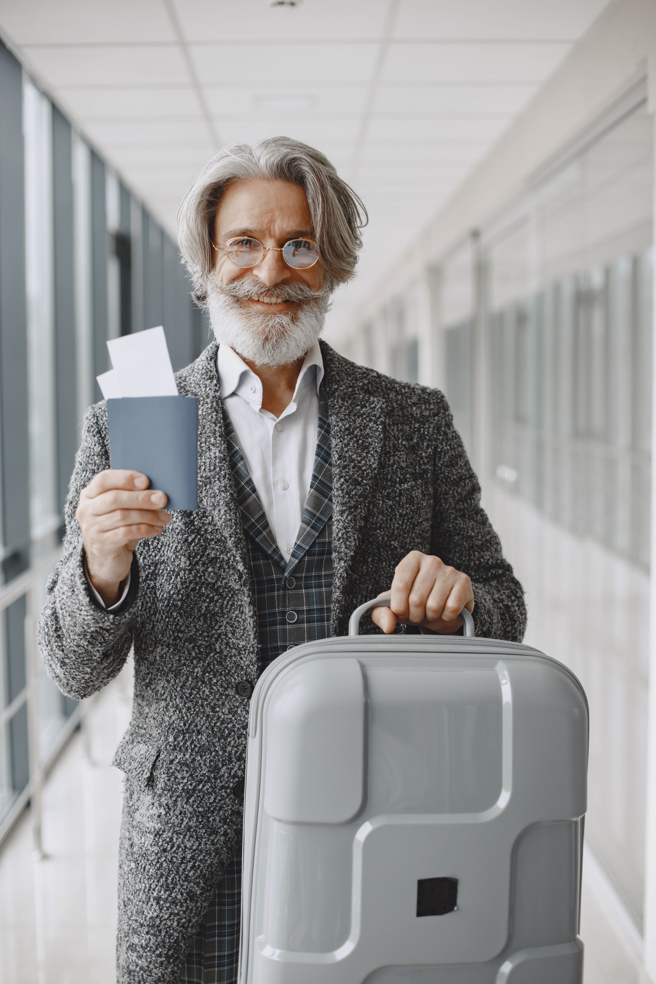 A smiling older man holding his passport and boarding pass, with a suitcase