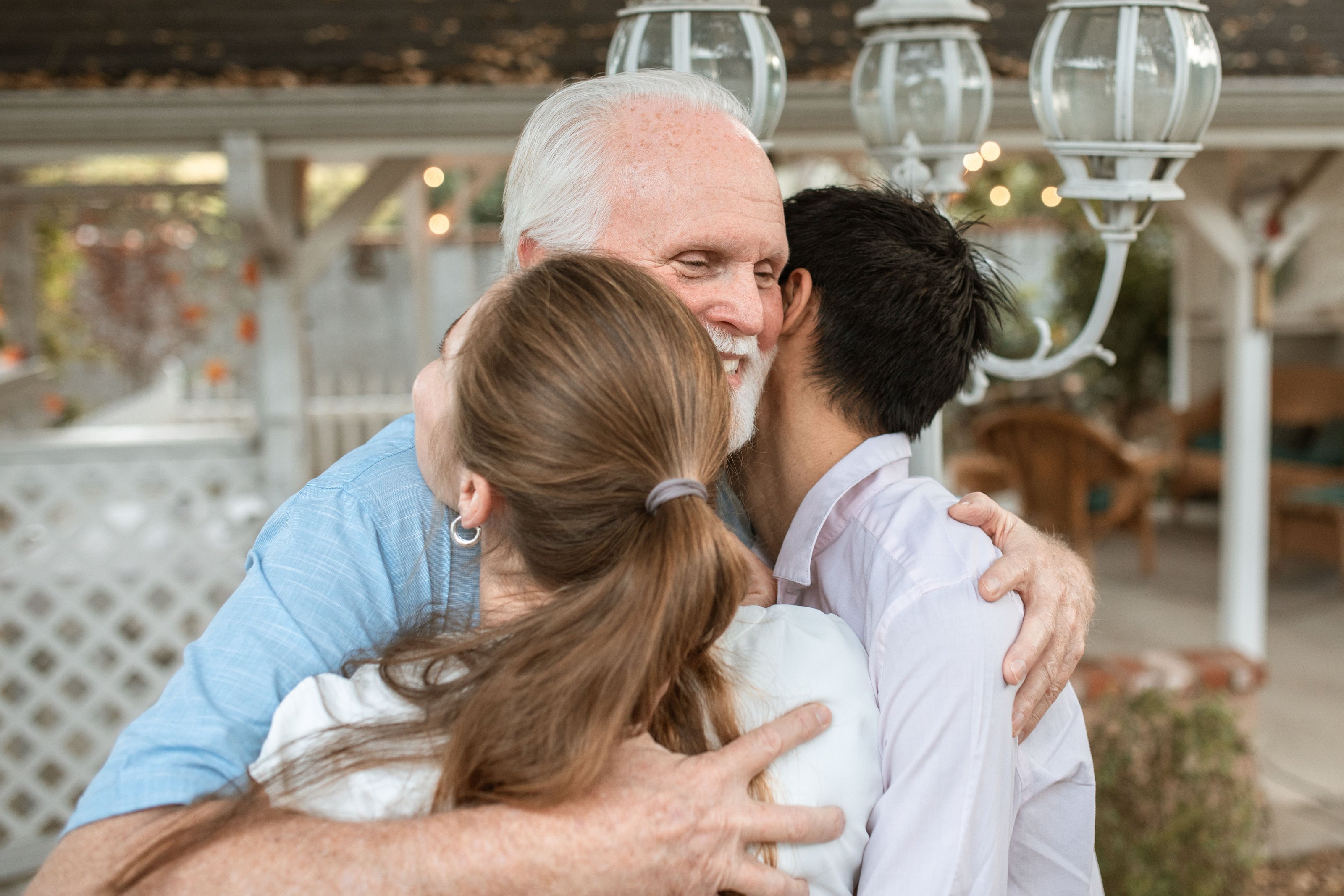 An older man hugging a younger couple on a porch